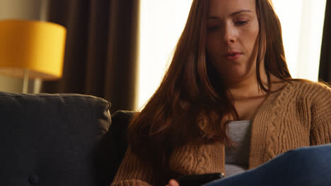 Close-Up-Of-Woman-Sitting-On-Sofa-At-Home-Using-Mobile-Phone-To-Check-Social-Media-Message-And-Scrolling-Online-1